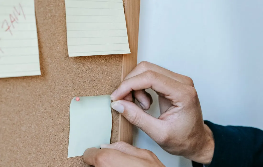 Anonymous hands pinning coloured notes to a noticeboard.