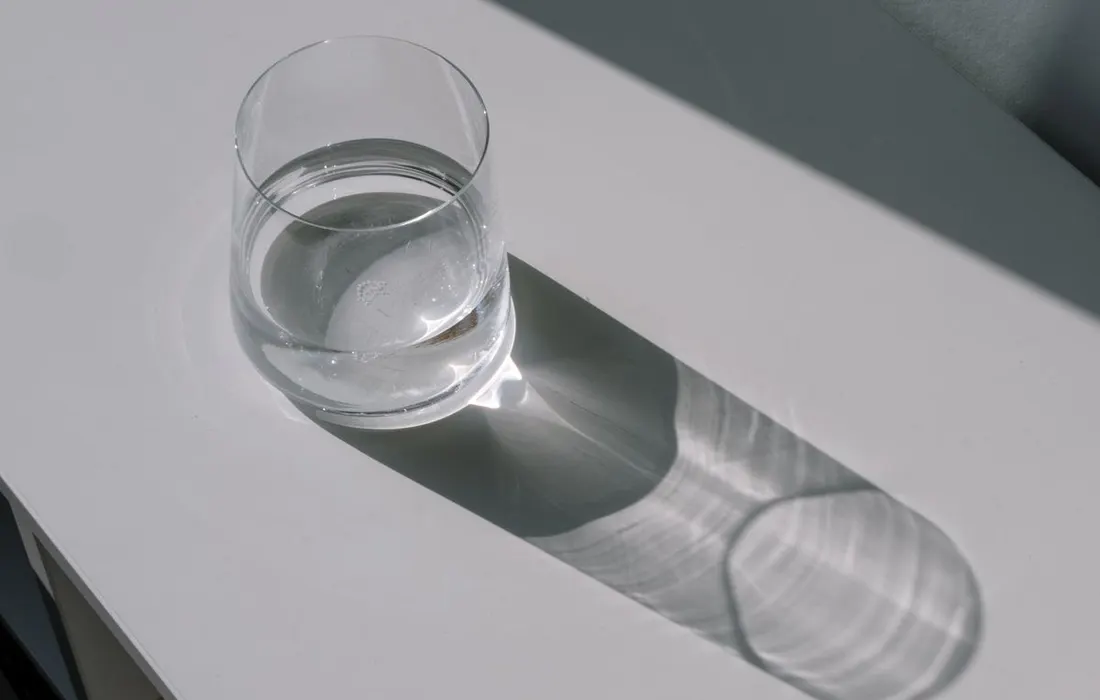 A clear glass of water casting a shadow on a white table.