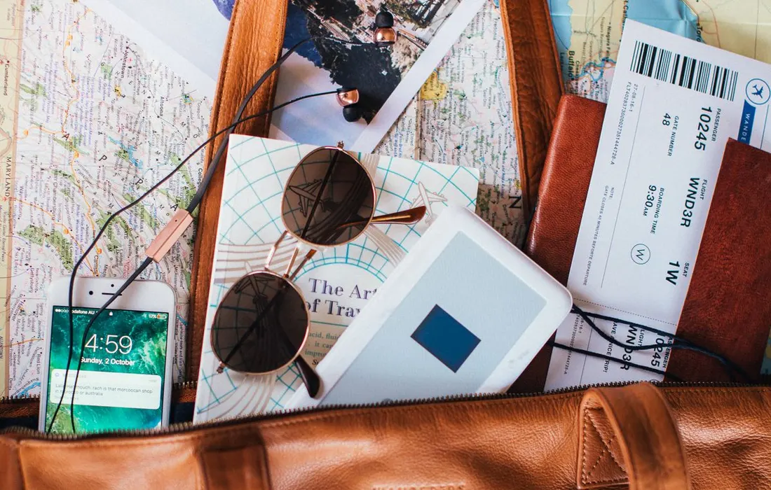 A travel bag with a paper map, sunglasses and travel tickets arranged beside it.