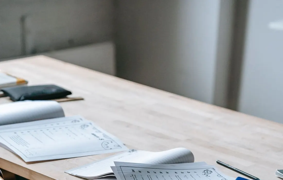 Schoolbooks and papers on a classroom desk with a backpack on the chair.