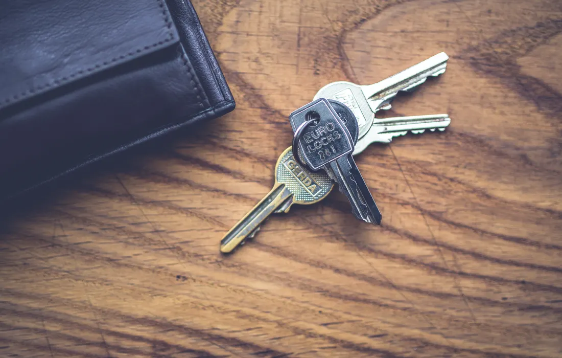 Keys and a black wallet on a wooden table.