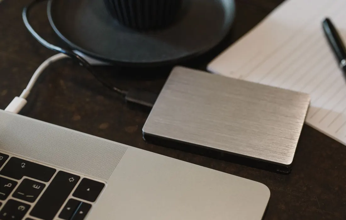 A portable storage drive connected to a laptop with a cable.