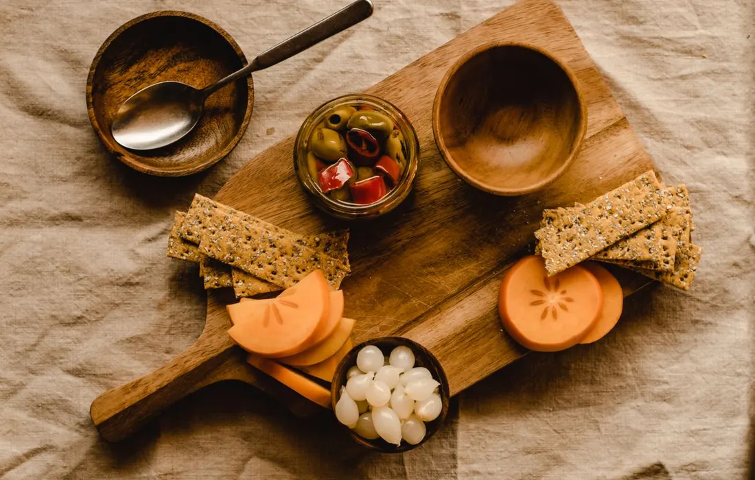 Crackers, olives and fruit arranged on a wooden board.