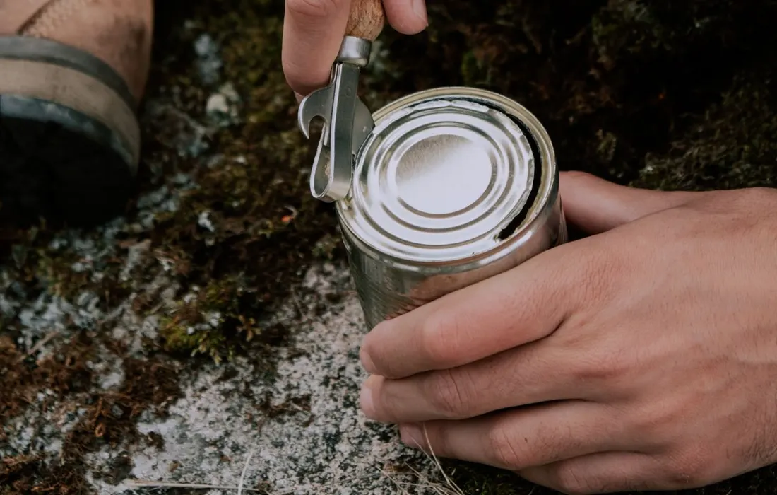 Hands using a manual opener on a tin outdoors.