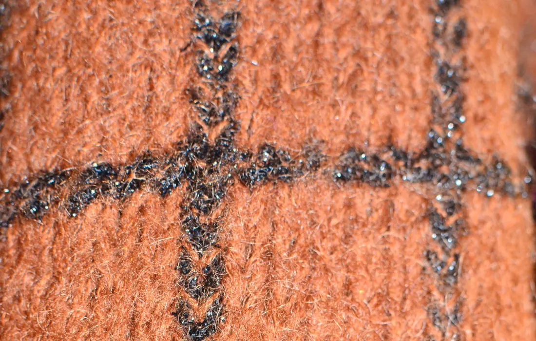 Closeup fragment of warm woolen blanket knitted with brown yarn forming checkered ornament and straight rows of thick black threads