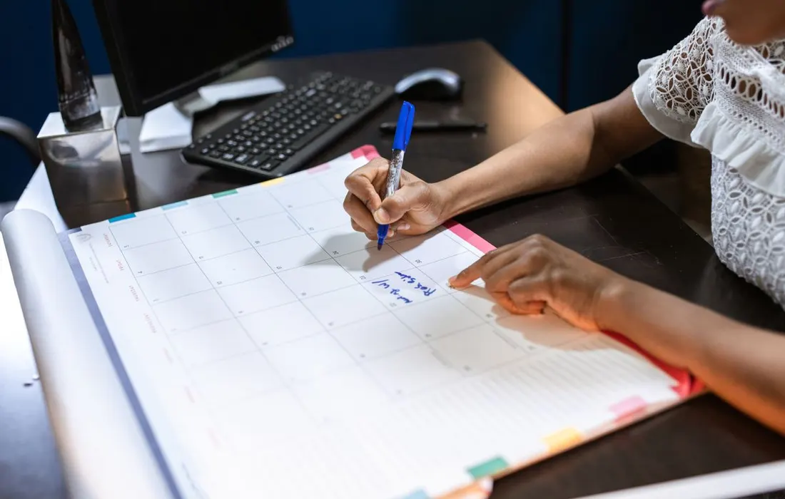 A hand writing notes in a paper desk calendar.