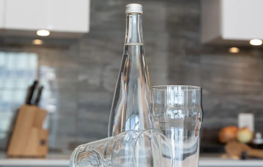 A glass water bottle and drinking glasses on a kitchen counter.