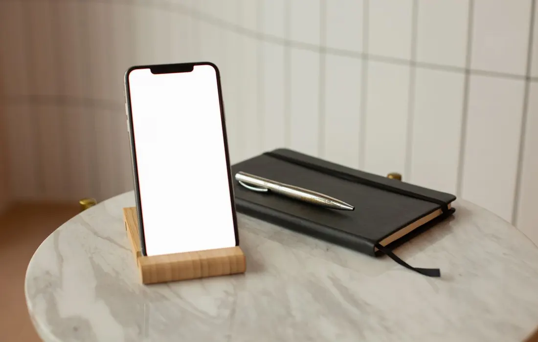 A smartphone with a blank screen beside a paper notebook.