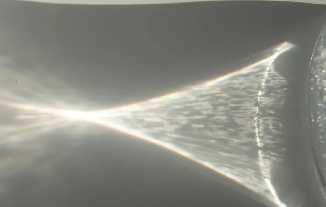 A glass of water casting a shadow on a white table.