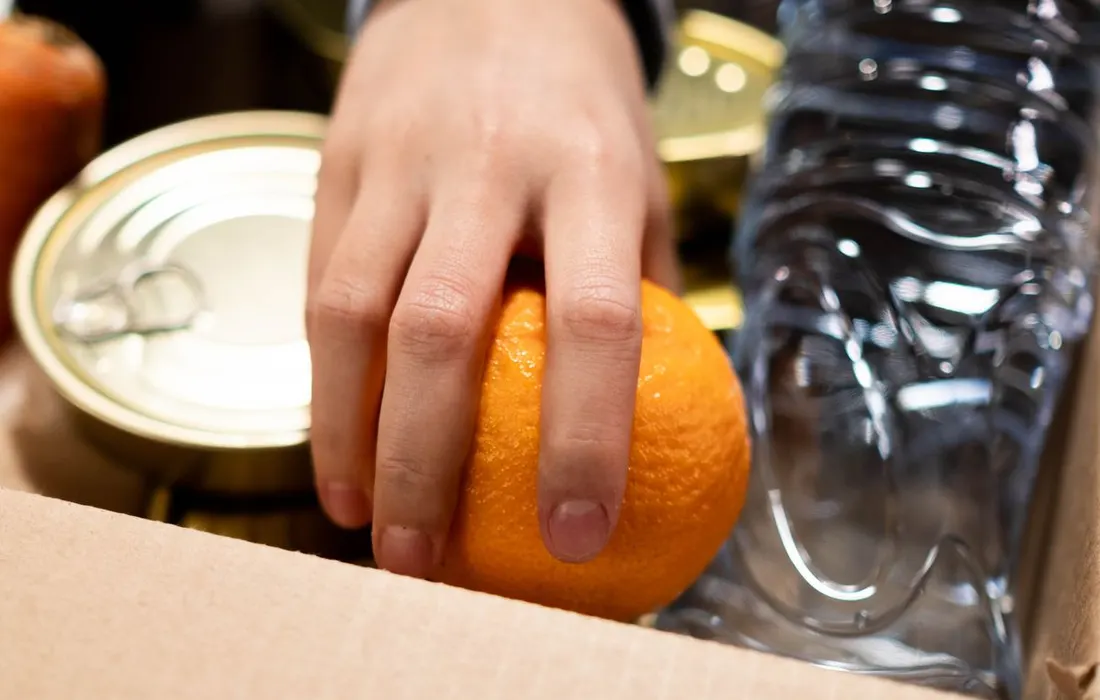A hand placing packaged food and bottled water into a box.