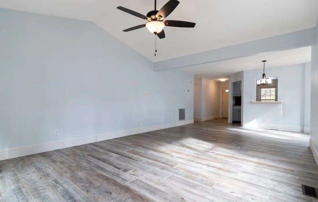 An empty living room with a wooden floor and ceiling fan.
