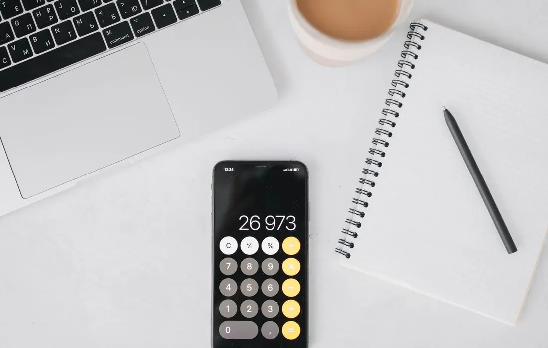 A laptop, notebook and phone showing a calculator on a desk.