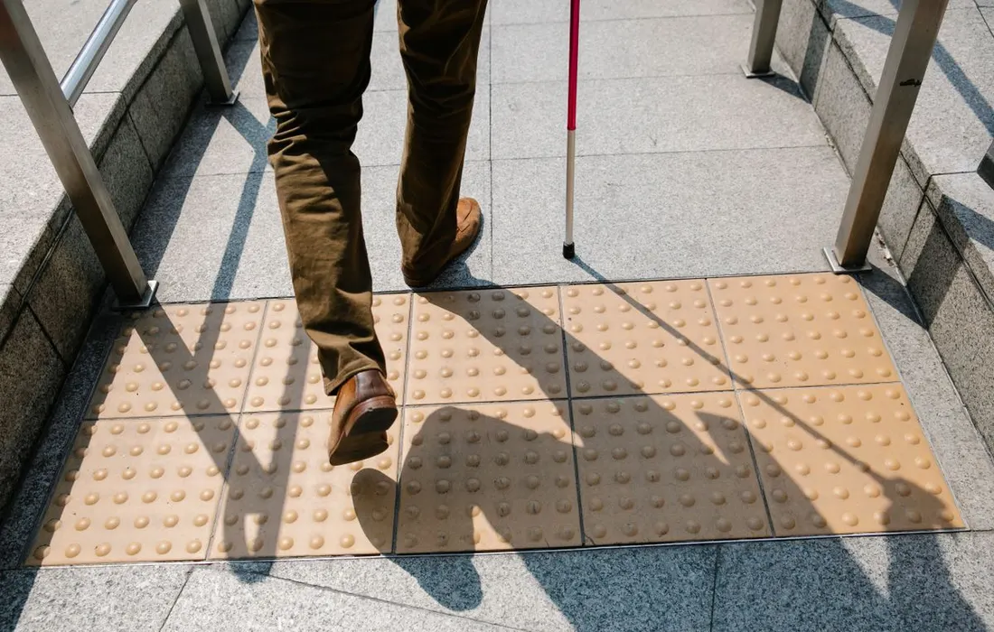 A person using a white cane beside tactile pavement markings.