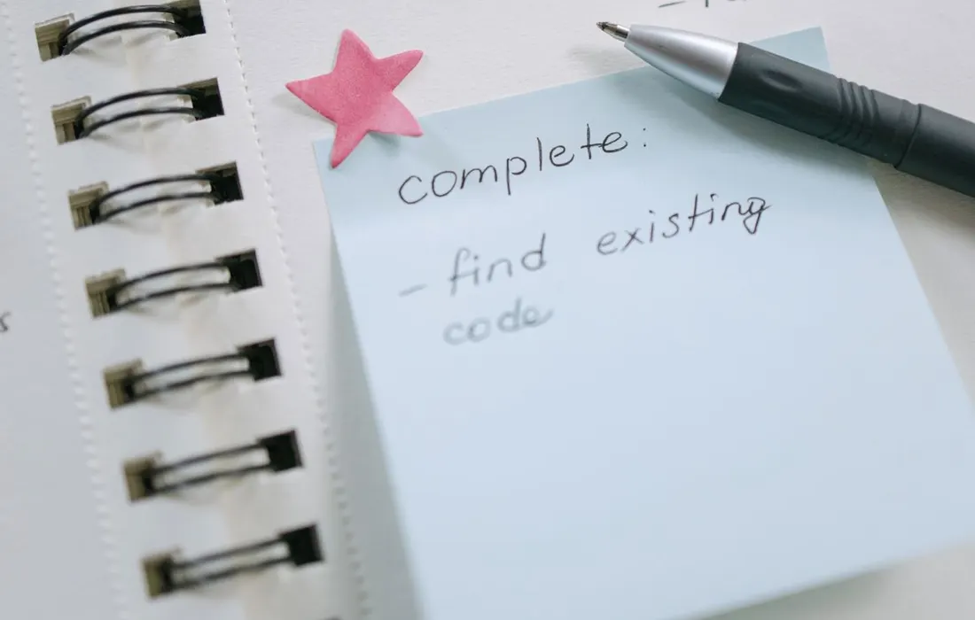 A pen, sticky notes and a handwritten list in a notebook.