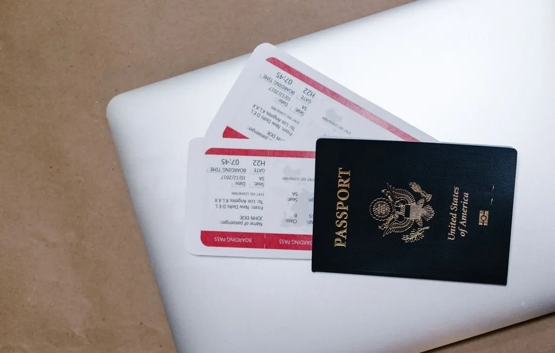 A passport and travel tickets resting on a laptop.