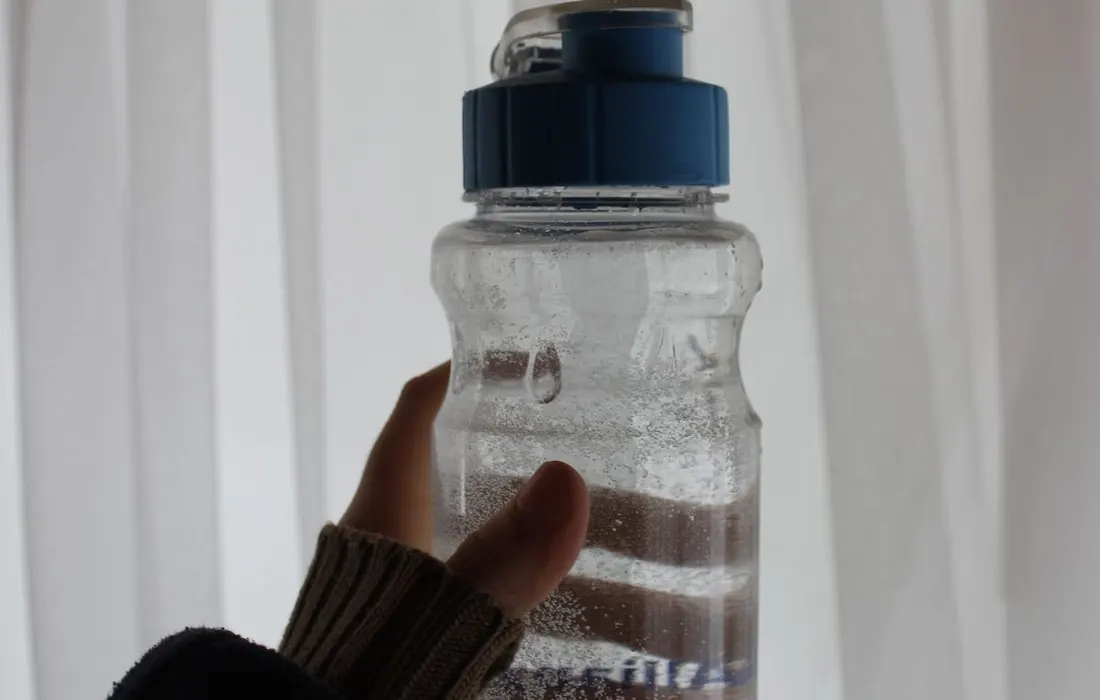 A hand holding a clear water bottle with a blue lid.
