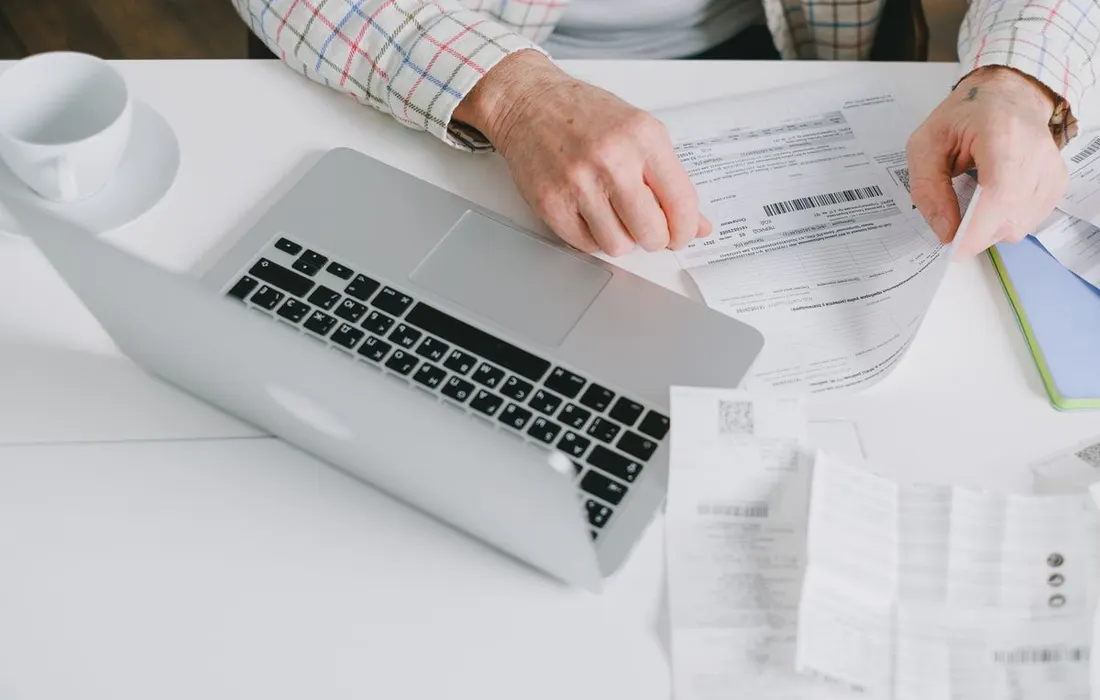Hands arranging printed documents beside a laptop.