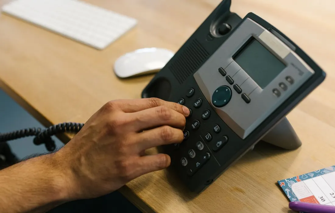 A hand dialling an office telephone beside a planner.