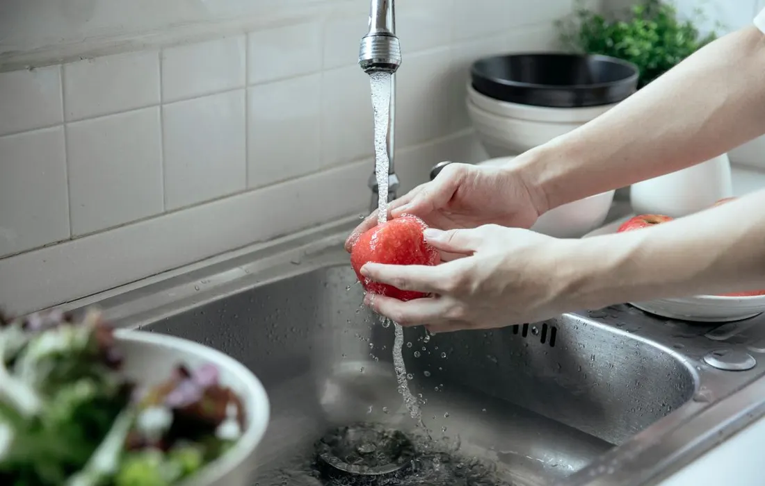 Hands washing an apple under a kitchen tap.