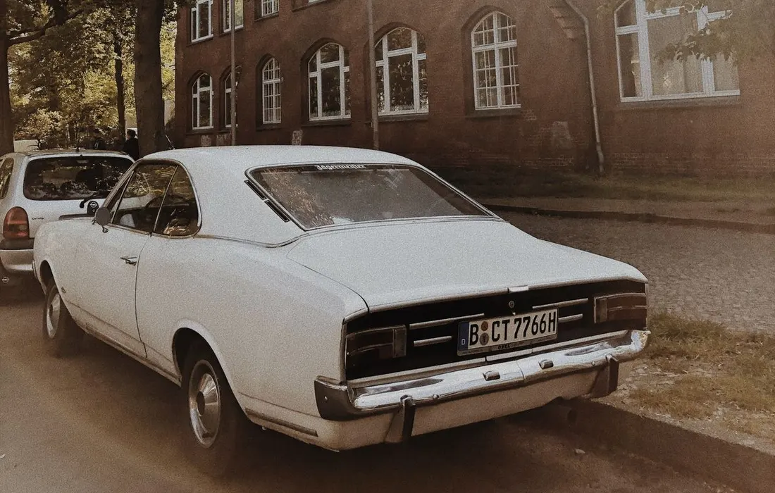 A parked car beside a brick building in sunlight.