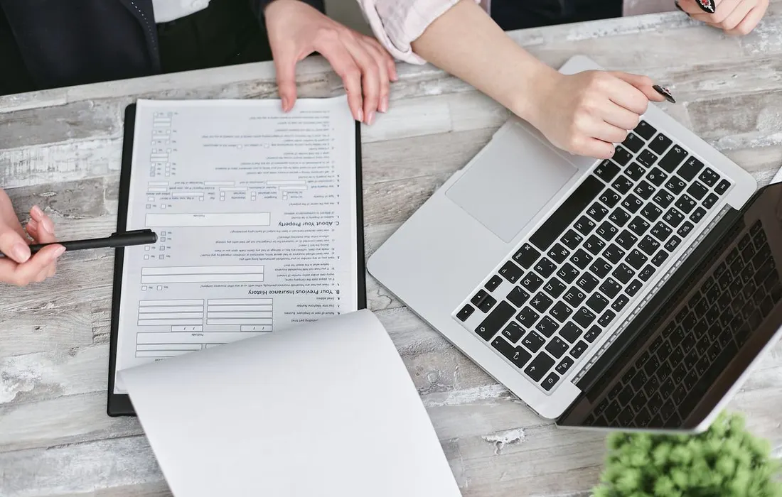Hands and documents beside a laptop during a planning discussion.