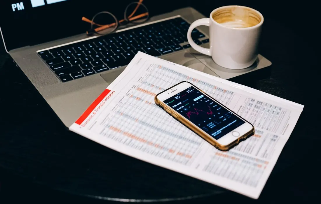 A smartphone, laptop and papers on a work table.