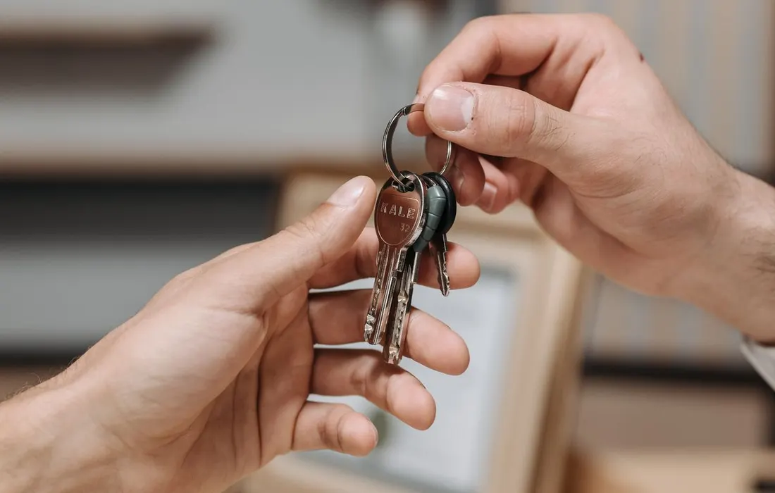 Two hands passing a set of keys indoors.