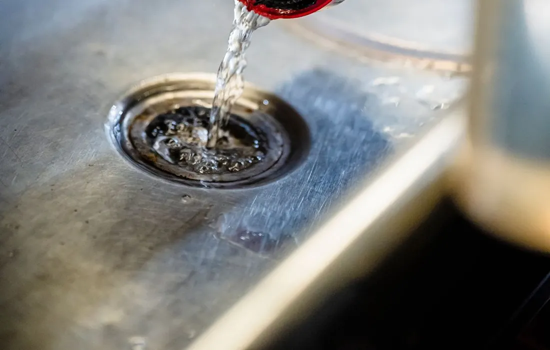 A hand tipping water from a plastic carrier into a sink.