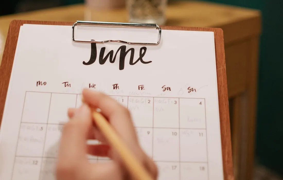 A hand marking a printed calendar on a clipboard.