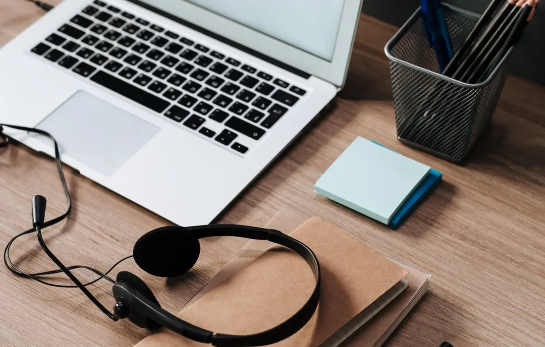 A work desk with a laptop, headset, notebooks and pens.