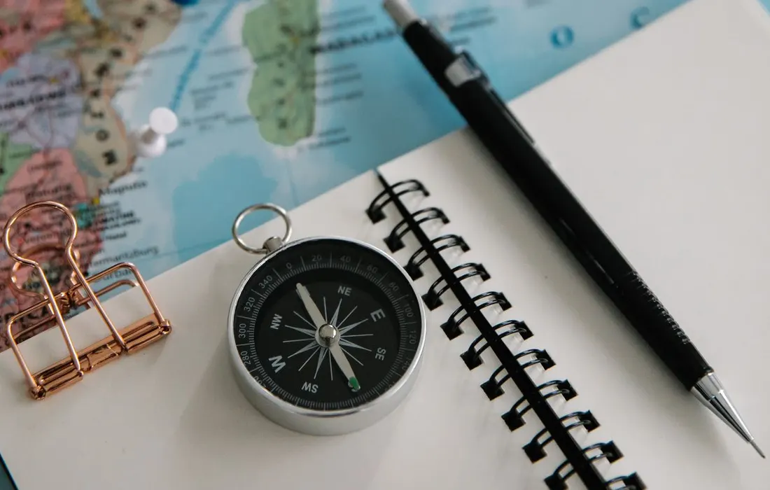 A notepad, pencil and compass arranged on a paper map.