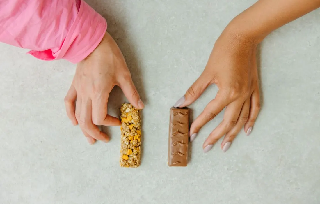 Hands holding a chocolate bar and a granola bar.