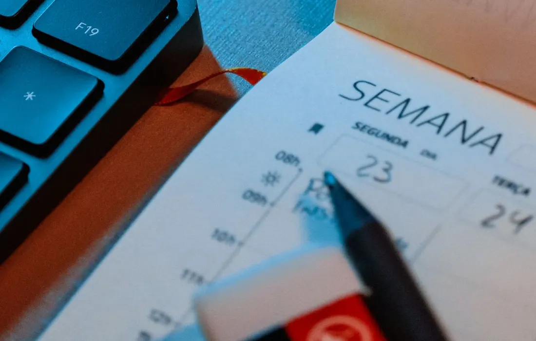 A weekly planner, pen and keyboard on a desk.