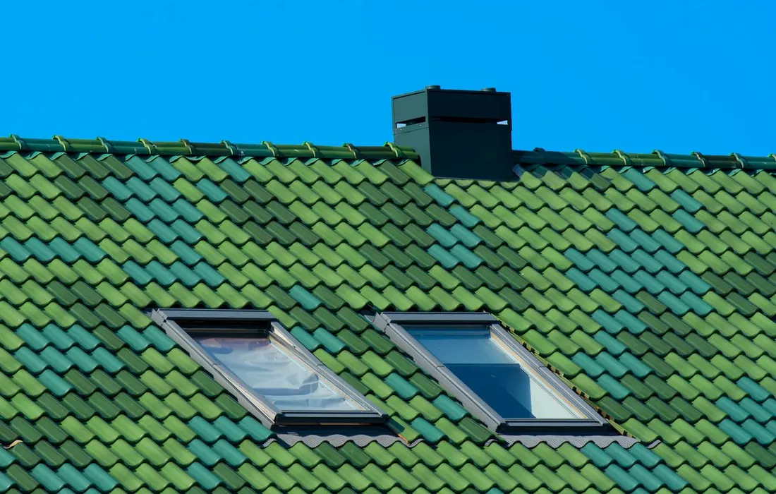 A house roof with a chimney and roof windows against a blue sky.