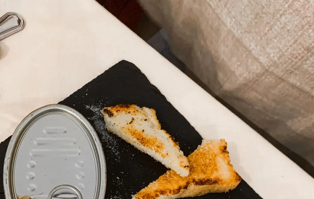 A small tin of fish served beside toast on a tray.