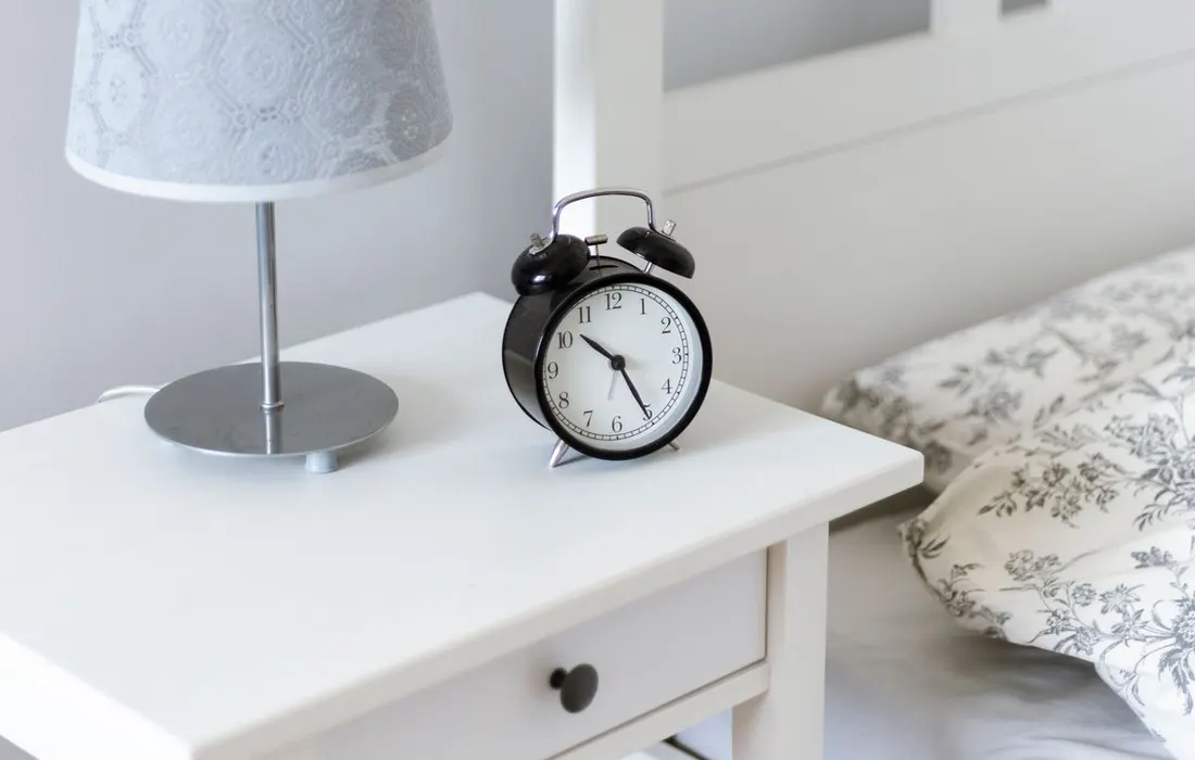 A bedside table with an alarm clock and a lamp.