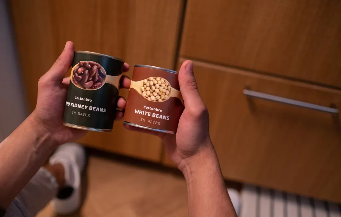 Hands holding two tins of beans in a kitchen.