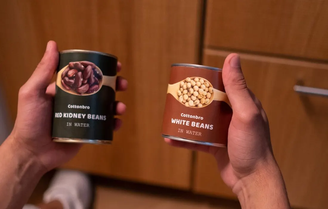 Hands holding tins of red kidney beans and white beans.