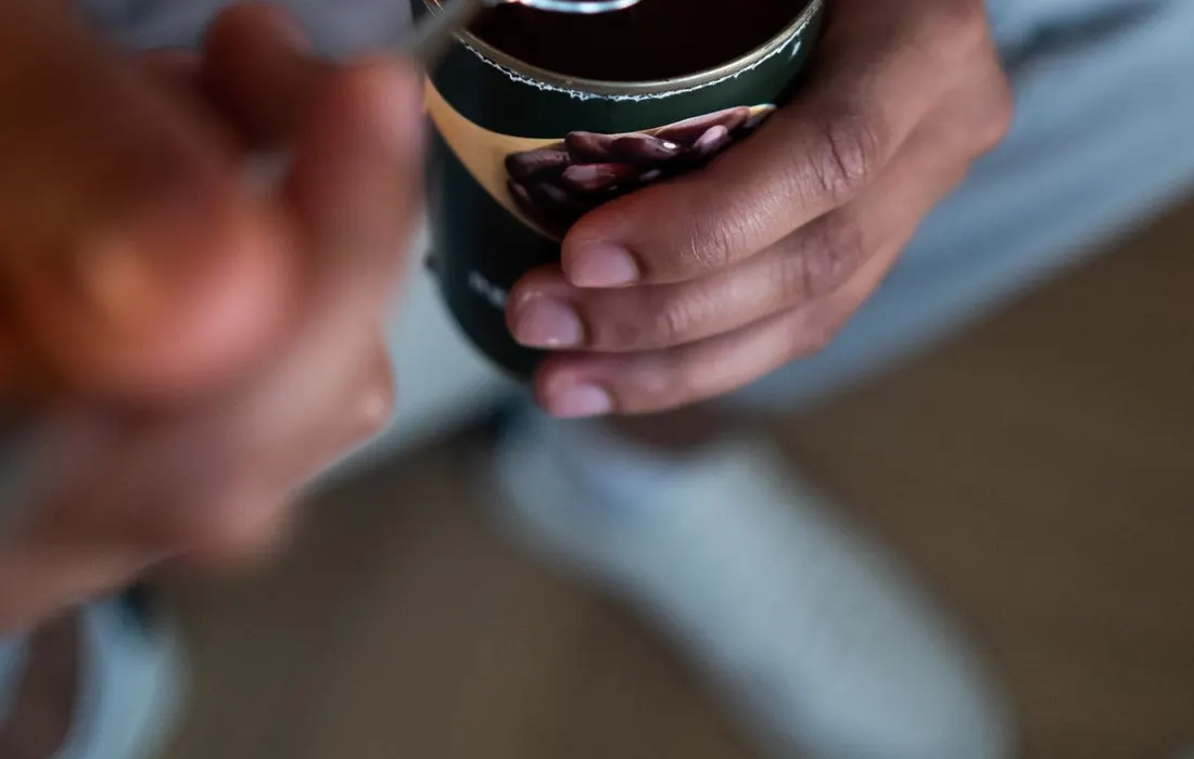 A hand holding a spoonful of beans above an open tin.